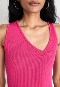 Dopasowany, prążkowany top na ramiączkach w jaskrawym różu, z głębokim dekoltem w kształcie litery V i szerokimi ramiączkami. Gładka faktura, minimalne detale szwów.