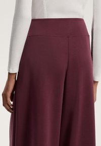Pantaloni largi de culoare vișinie cu o textură netedă și talie elastică. Țesătura coboară ușor și are o culoare uniformă, fără modele.
