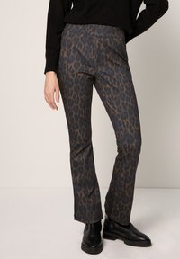 Leopardikuvioidut liehuvat housut, joissa on sileä rakenne tummanruskeissa ja mustissa sävyissä, yhdistettynä mustiin nilkkureihin ja mustaan neulepaitaan.