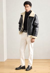 Czarna skórzana kurtka z beżowym sztucznym kołnierzem z baranka, zestawiona z czarnym golfem, białymi spodniami i czarnymi mokasynami.