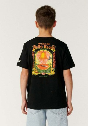 Junge mit kurzen braunen Haaren, der ein schwarzes T-Shirt mit einem bunten Bell's Beach Australien-Motiv und hellblaue Shorts trägt, von hinten gesehen.