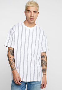 White short-sleeve t-shirt with vertical black stripes, crew neck, relaxed fit, soft cotton texture, displayed with denim jeans.