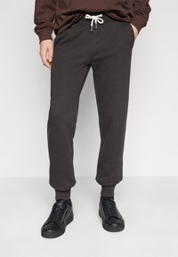 Dunkelgraue Sweatpants mit einem Kordelzugbund, enganliegenden Bündchen und Seitentaschen, kombiniert mit schwarzen Turnschuhen. Weiche, glatte Stofftextur.