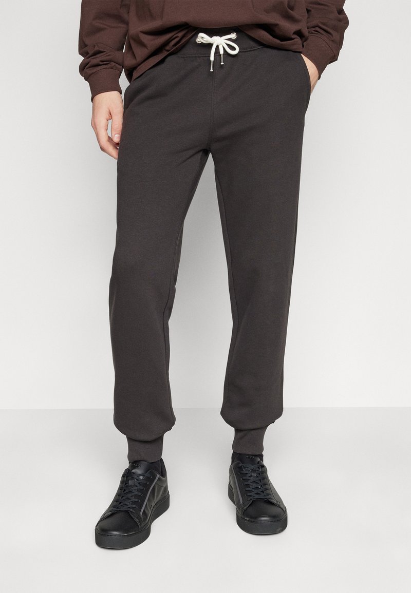 Dunkelgraue Sweatpants mit einem Kordelzugbund, enganliegenden Bündchen und Seitentaschen, kombiniert mit schwarzen Turnschuhen. Weiche, glatte Stofftextur.