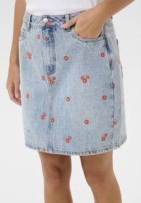 Jupe en denim bleu clair avec des broderies florales rouges. Présente une taille ajustée, deux poches latérales et une légère forme évasée.