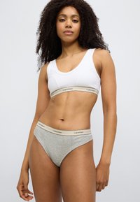 Λευκό βαμβακερό crop top με κυρτή γραμμή στο λαιμό και ελαστική ζώνη μέσης με λογότυπο Calvin Klein, συνδυασμένο με ανοιχτό γκρι βαμβακερά εσώρουχα που διαθέτουν αντίστοι χη ζώνη με λογότυπο.