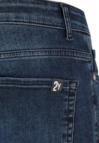 Tamno plave traperice sa stražnjim džepom na kojem se nalazi pravokutna crna oznaka s natpisom "2Y." Glatka tekstura s vidljivim detaljima šivanja.