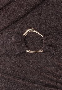 Gros plan d'une boucle en métal bronze brillant sur une ceinture en tissu texturé foncé avec un effet pailleté subtil.