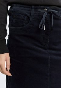 Jupe en velours côtelé bleu foncé avec taille à cordon, poches avant et tissu texturé. Présente une coupe ajustée et un motif côtelé discret.