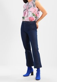 Blusa rosa floral con mangas cortas, vaqueros de cintura alta azul oscuro y botas de tobillo azules lisas con tacón cuadrado.