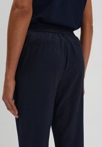 Pantalons de jogging bleu marine avec une taille à cordon de serrage et deux poches arrière, présentant une texture lisse et une conception de jambe fuselée.