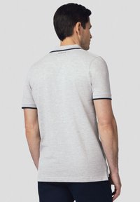 Szara koszulka polo z teksturowanej tkaniny, z krótkimi rękawami i granatowymi akcentami na kołnierzyku oraz brzegach rękawów. Widok z tyłu pokazujący metkę.