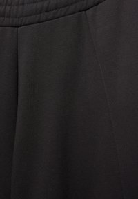 Tkanină sport neagră, cu o textură netedă, având un tiv plat și detalii de cusătură subtile, care evidențiază designul drapat al articolului.