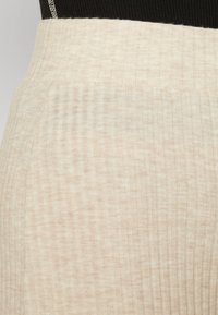 Tessuto a coste di un beige chiaro con sottili variazioni di texture, superficie liscia e una cintura elastica.
