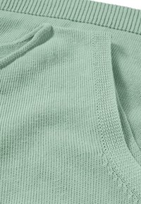 Hellgrüner Strickstoff mit einem gerippten Bund, der eine glatte Textur und gleichmäßige Nähte aufweist, wodurch seine weiche und atmungsaktive Qualität betont wird.