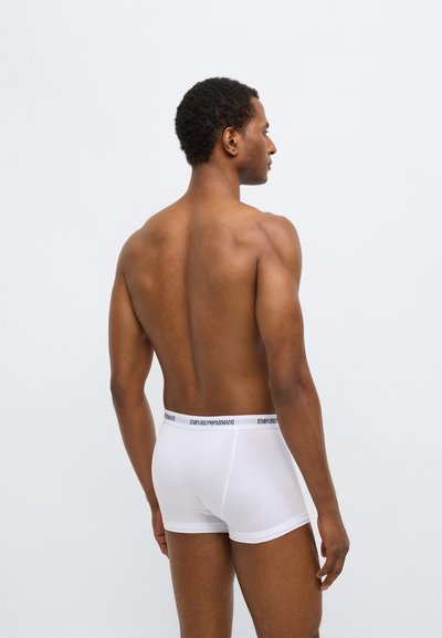 Boxers en coton blanc avec une ceinture noire à logo, vus de dos, mettant en valeur la texture lisse et la coupe ajustée.