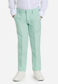 Pantaloni verde menta con frontale piatto, tasche laterali e vestibilità sartoriale, abbinati a sneakers bianche e una camicia bianca a maniche lunghe.