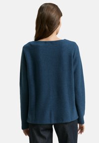 Blauer Strickpullover mit lockerer Passform, weitem Ausschnitt und langen Ärmeln. Texturiertes Material mit glatter Oberfläche, endet auf Hüfthöhe.