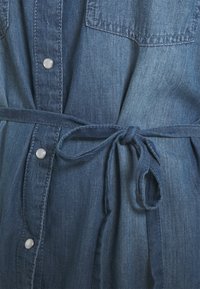 Jeansklänning med två bröstfickor, silverknappar, ett knytbälte i midjan och en gradient blå färgschema med en mjuk textur.