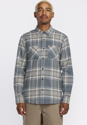 Plaid button-up shirt in gray, cream, and mustard colors. Features two front pockets and a standard collar. Made of a soft fabric.