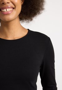 Sort langærmet top med rund halsudskæring og tætsiddende design, lavet af et glat, blødt materiale. Har et rent, minimalistisk udseende.