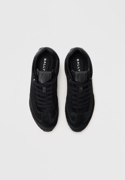 Baskets noires en mélange de suède et de matériau texturé, avec des lacets plats, un logo en relief sur la languette et une silhouette athlétique classique.