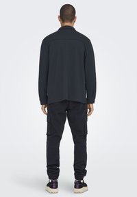 Svart långärmad skjorta med rak fåll, kombinerat med cargobyxor med flera fickor och sneakers med en strukturerad sula.