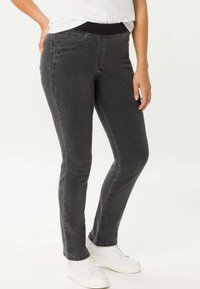 Graue Jeans mit schlanker Passform, ausgestattet mit einem schwarzen elastischen Bund und Vordertaschen, kombiniert mit weißen Sneakern.