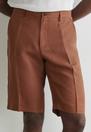 Braune, maßgeschneiderte Shorts bis zum Knie mit Knopf- und Reißverschluss, getragen mit einem weißen Stricktop.