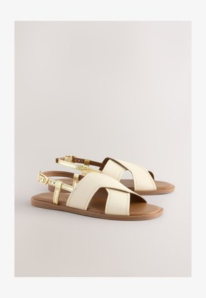 Kreemivärvi naha plätud kuldsete detailidega. Avatud varbaga disain, reguleeritavad pahkluu rihmad ning lamedad pruunid tallad. Vabaaja ja minimalistlik stiil.