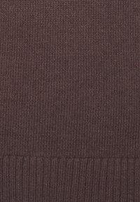 Dunkelbrauner gestrickter Stoff mit einer gerippten Textur. Die Oberfläche weist ein gleichmäßiges Stichmuster auf, das ein warmes, dichtes Erscheinungsbild erzeugt.