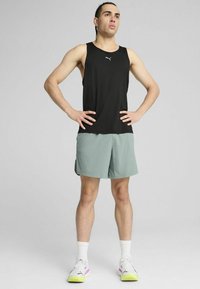 Crna majica bez rukava s logom, uparena s svijetlozelenim šortsevima. Outfit dodatno naglašavaju bijele čarape i sportske tenisice s kolorističkim naglascima.