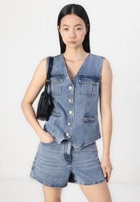 Denim ermeløs vest med V-hals, frontknapper og to brystlommer; kombinert med matchende denimshorts. Lys blå vask, uformell passform.