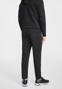 Czarny zestaw dresowy z bluzą i spodniami, wykonany z teksturowanej tkaniny, z kapturem, tylną kieszenią i trampkami z kontrastującą białą podeszwą.