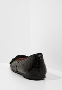 Svart ballerinaskor med ett texturerat svarmönster, med en björkaccents och en låg, rund sula. Slät, glänsande yta.