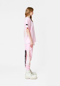 Camiseta gráfica rosa de manga corta con bordado en las mangas, y joggers rosas con un bordado similar y una etiqueta negra en el lateral. Botas blancas.