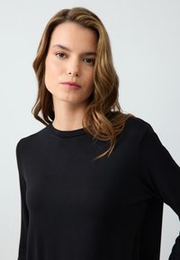 Zwarte lange mouwen top van soepel materiaal met een ronde halslijn en een relaxed fit, met minimale details en een gelijkmatige textuur.
