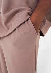 Helles Mauve-Set aus strukturiertem Stoff. Das Oberteil hat eine lockere Passform mit einer Tasche; die Hose hat ein ausgesticktes Logo an der Seite.