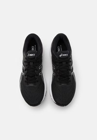 Baskets de sport noires avec une tige en mesh, surface texturée, accents blancs et semelle rembourrée. Présente un design à lacets et un détail de logo.