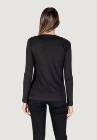 Schwarzes Langarmshirt aus leichtem Stoff mit figurbetontem Schnitt. Verfügt über einen Rundhalsausschnitt und nahtlose Rückenstiche. Kombiniert mit dunklen Jeans.