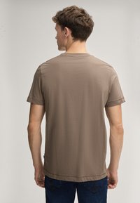 Bruine t-shirt met korte mouwen van zacht stof, met een ronde hals en een rechte zoom, gedragen met blauwe denim jeans.