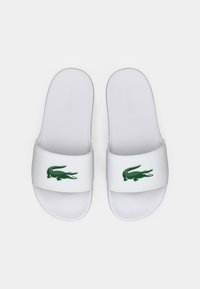 Hvide sliders med et grønt krokodillelogo på remmen. Fremstillet af glat syntetisk materiale med et fladt således design.