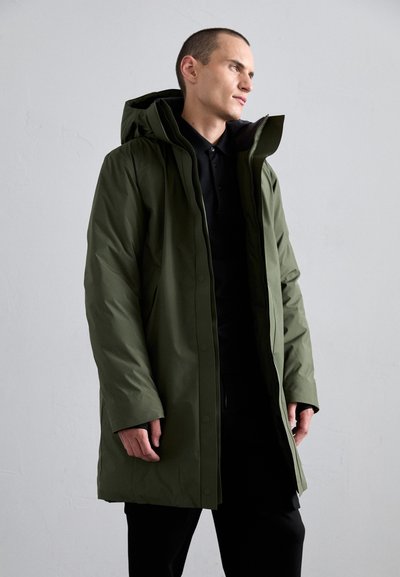 Green waterproof parka with a hood, front zipper, and button closures. Fabric appears smooth with a relaxed fit, layered over a black shirt.