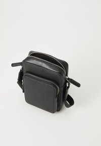 Sort læder crossbody-taske med to lynlåslommer, der har en tekstureret overflade og sorte metaldele. Kompakt firkantet design.