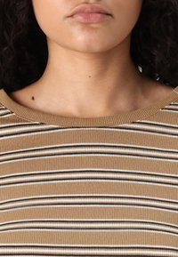 Lys ribbet topp med horisontale striper i brunt og hvitt. Har en vid utringning og en glatt tekstur.