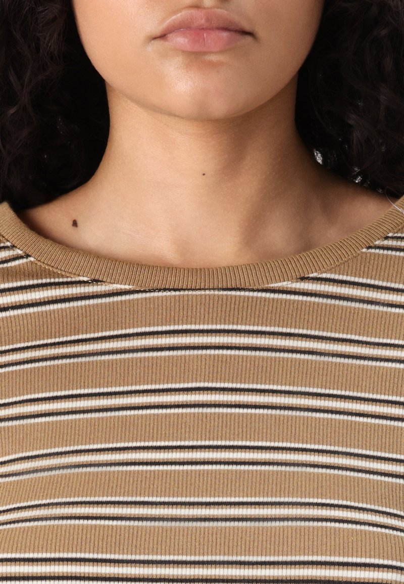 Haut côtelé beige avec des rayures horizontales marron et blanc. Il dispose d'un large col et d'une texture lisse.