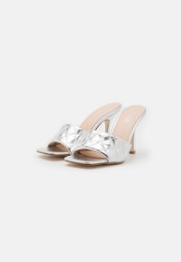 Zilveren, gequiltte muiltjes met een open teen, voorzien van een hoge hak en een gladde metallic afwerking. De binnenzool is van een zachte, nude kleur.