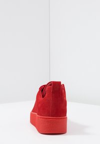 Baskets en daim rouge avec une semelle haute texturée, bout rond et détail de marque discret au talon, conçues pour un usage décontracté.