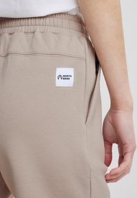 Bežové jogger nohavice s elastickým pásom, ktoré majú biely štítok s logom "NORTH BEND" a bočné vrecko so zipsom.