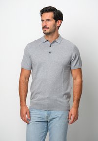 Grå kortärmad polo med krage och tre knappar; gjord av ett strukturerat stickat tyg; matchad med ljusblå jeans.